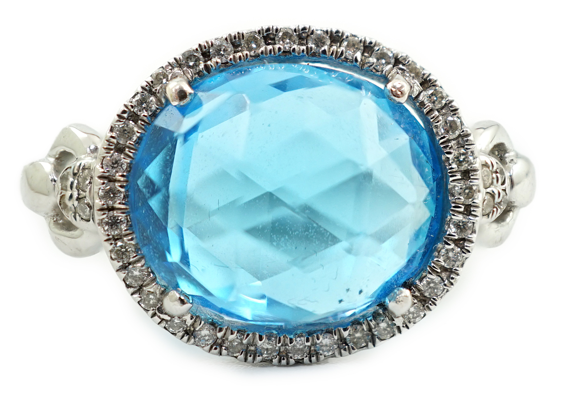 A modern 18ct white gold and facetted oval cut blue topaz set dress ring, with diamond chip set border and shoulders